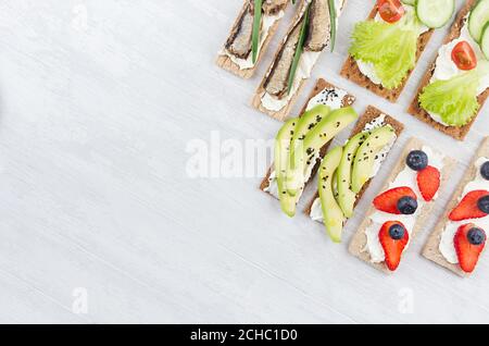Gesunde diätetische Auswahl an Chips Roggen flache Toast mit frischem Gemüse, reifen Früchten, Fischkonserven, Frischkäse auf weißem Holz Hintergrund, Top vie Stockfoto