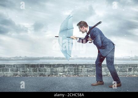 Geschäftsmann mit Regenschirm steht vor starkem Gegenwind Stockfoto