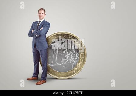 Geschäftsmann, der neben einer übergroßen Euro-Münze steht Stockfoto
