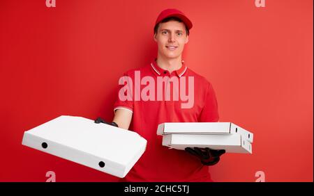 Handsome kaukasischen Delivery Mann hält Pizza in Box isoliert über roten Studio Hintergrund, Lieferung während Quarantäne Coronavirus Konzept. Stockfoto