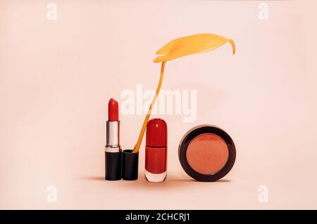 Dekorative Komposition mit Kosmetik, Frauen-Beauty-Produkte, roter Lippenstift, Rouge und Nagellack, verziert mit Herbstgelb Blatt auf hellem Hintergrund, Mode Stillleben Stockfoto