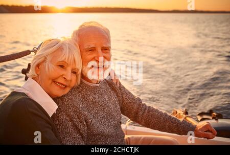 Portrait eines schönen und glücklichen älteren Paares in der Liebe Umarmung, Entspannung und Lächeln während Segeln zusammen im Meer bei Sonnenuntergang, genießen erstaunlich Stockfoto
