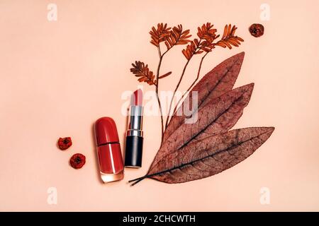 Dekorative flache Lay-Komposition mit Kosmetik, Frauen-Beauty-Produkte, roten Lippenstift, Nagellack, mit Herbstblättern und Beeren verziert. Flach liegend, Draufsicht auf hellem Hintergrund, Mode Stillleben Stockfoto