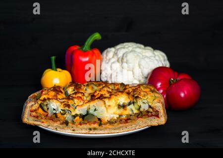 Gemüsekuchen in Nahaufnahme mit einem Satz Gemüse für die Herstellung der Füllung auf einem dunklen Holzhintergrund. Das Konzept des Kochens. Stockfoto