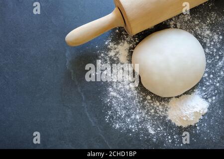 Teigkugel mit Nudelholz für Knödel oder Nudeln auf dem Steinbrett. Teig mit Mehl, Eiern, Salz. Roher Teig.hausgemachtes Backen. Stockfoto