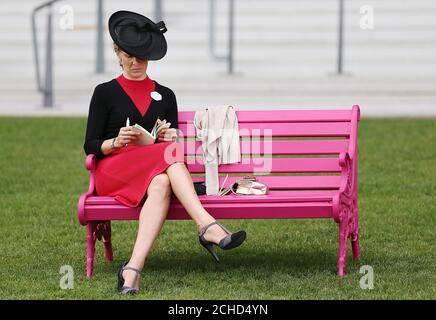 Eine weibliche Rennfahrerin liest eine Rennkarte auf einer rosa Bank während des zweiten Tages von Royal Ascot auf der Ascot Rennbahn. Stockfoto