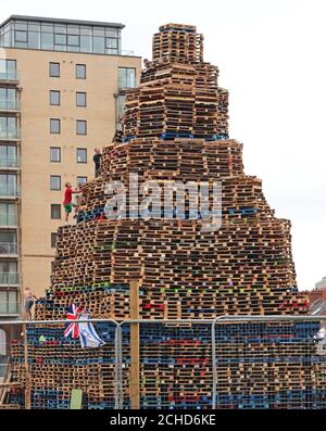 Lagerfeuerbauer in der Sandy Row-Gegend von Belfast, als die Bereitschaftspolizei maskierte Auftragnehmer eskortierte, als sie Holz von zwei umstrittenen loyalistischen Lagerfeuerstellen in Belfast entfernten. Stockfoto