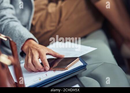 Die Aufnahme einer Geschäftsfrau in klassischer Kleidung, die auf dem Rücksitz im Auto sitzt und ihr Smartphone, ihr Geschäft und ihre Technologien benutzt Stockfoto