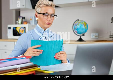 Blonde kaukasische weibliche junge Schullehrerin mit Webcam zu Hause, virtuelles Unterrichtskonzept, geben Remote-Klasse Online-Unterricht per Zoom Konferenzgespräch Stockfoto