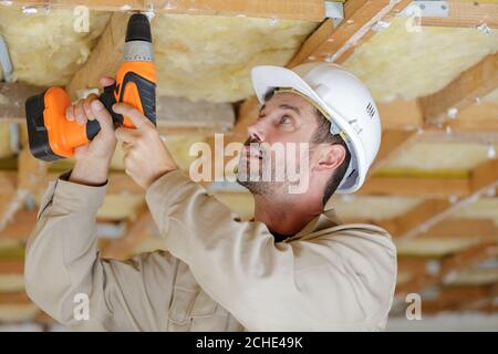 baumeister mit Akku-Bohrer auf Holzdeckenbalken Stockfoto