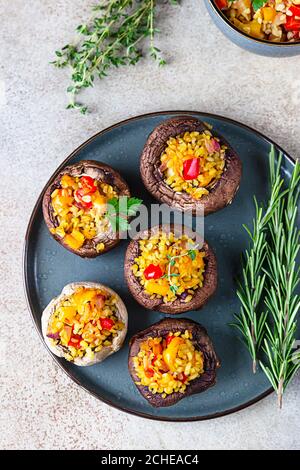 Gebackene gefüllte portobello-Pilze mit Bulgur-Pilaf und gehacktem Gemüse. Leckeres und nahrhaftes vegetarisches Gericht. Steinhintergrund, selektiver FOC Stockfoto