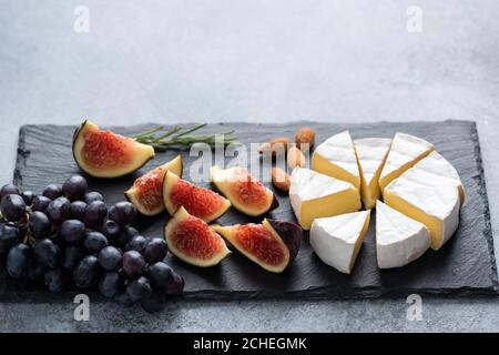 Brie Käse mit Feigen und Trauben auf schwarzem Schiefer. Gourmet-Käseplatte Stockfoto