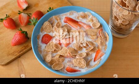 Vollkornflocken mit Milch und Erdbeeren in blauer Schale auf Holztisch. Gesundes Frühstück Stockfoto