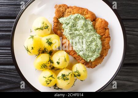 Deutsches Kalbsschnitzel mit gekochten neuen Kartoffeln und grüner Soße in einem Teller auf dem Tisch. Horizontale Draufsicht von oben Stockfoto