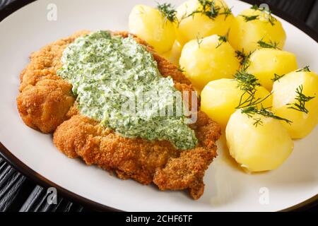Deutsches Kalbsschnitzel mit gekochten neuen Kartoffeln und grüner Soße in einem Teller auf dem Tisch. Horizontal Stockfoto
