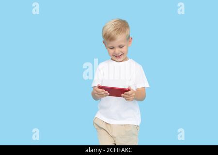 Niedliche smilling Kind Junge mit Smartphone auf blauem Hintergrund. Werbung für pädagogische Anwendungen auf einem Handy für Kinder. Lustiges Gesicht. Stockfoto