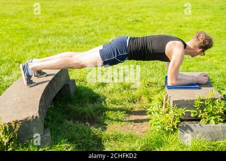 Junger Mann, der Plank-Übung in einer Außenumgebung durchführt. Stärkung der Kernmuskulatur, Bewegung, fit halten, Gesundheit Stockfoto