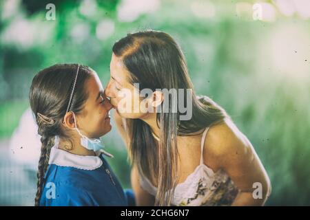 Junges Mädchen trägt Gesichtsmaske Rückkehr in die Schule nach Pandemie. Küssen ihre Mutter verlassen zu Hause. Stockfoto