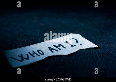 Ein Stück Papier mit der Frage, wer ich darin geschrieben bin, auf einer schwarzen strukturierten Oberfläche Stockfoto