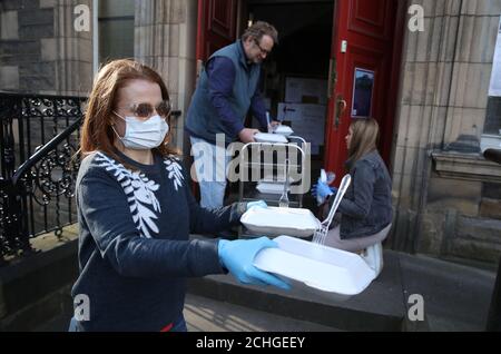 Der Freiwillige Lindsay Scott von der Step to Hope Wohltätigkeitsorganisation in Edinburgh überreicht zusammen mit Rev. Peter Sutton von der Pfarrkirche St. Cuthbert in Edinburgh Mahlzeiten an Obdachlose. Normalerweise werden Mahlzeiten in der Kirche serviert, aber aufgrund von Einschränkungen werden diese außerhalb an die Obdachlosen übergeben, da Großbritannien weiterhin in Lockdown, um die Ausbreitung des Coronavirus einzudämmen. Stockfoto