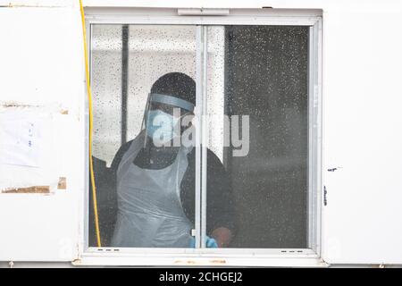 Ein Tester mit persönlicher Schutzausrüstung (PSA) blickt aus einem Fenster auf eine Fahrt durch die Coronavirus-Teststelle bei IKEA in Wembley, Nord-London. Stockfoto