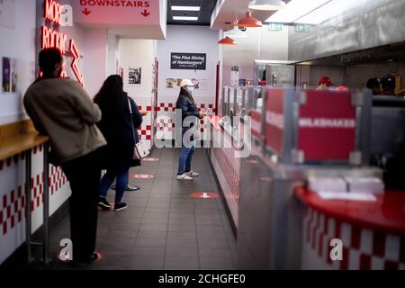 Die Kunden bleiben in sozialer Distanz, während sie warten, bis sie im Restaurant Five Guys in Kensington, London, Bestellungen abholen, nachdem die Burger-Kette acht ihrer Standorte wiedereröffnet hat, während Großbritannien weiterhin gesperrt wird, um die Ausbreitung des Coronavirus einzudämmen. Stockfoto