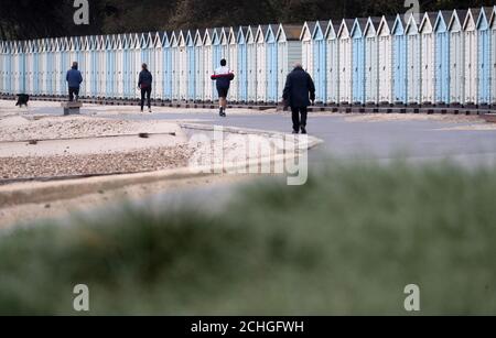 Die Menschen machen sich auf den Weg, vorbei an Strandhütten am Avon Strand in Christchurch, Dorset. Stockfoto