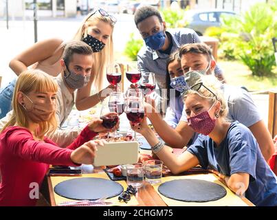 Freunde mit Gesichtsmaske nehmen Selfie beim Toasten Rotwein Im Restaurant - Junge Leute, die Spaß mit Getränken haben - Das neue normale Lifestyle-Konzept Stockfoto