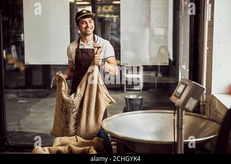 Fröhlicher junger Mann hält Beutel mit Kaffeebohnen Stockfoto