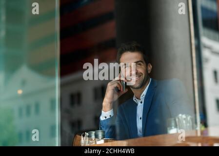 Lächelnder Geschäftsmann, der sich in einem Café mit seinem Handy unterhielt Stockfoto