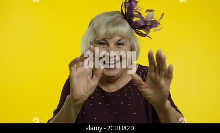 Porträt einer freundlichen positiven älteren alten blonden Frau winkende Hände Blick auf die Kamera mit toothy Lächeln, sagen Hallo, Gruß. Ältere stilvolle Dame Oma auf gelbem Hintergrund im Studio Stockfoto