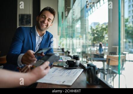 Lächelnder Mann, der seinen Kellner mit nfc-Technologie bezahlt Stockfoto