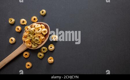 Pasta-Kochkonzept. Frische hausgemachte Tortellini auf einem Holzlöffel, schwarzer Stein Hintergrund, Draufsicht, Kopierraum Stockfoto