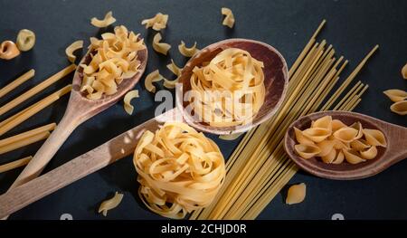 Pasta-Kochkonzept. RAW Pasta verschiedene Formen und Löffel auf schwarzem Stein Hintergrund, Nahaufnahme Stockfoto