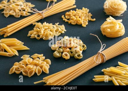 Pasta-Kochkonzept. RAW Pasta Formen Vielfalt auf schwarzem Hintergrund, Nahaufnahme Stockfoto