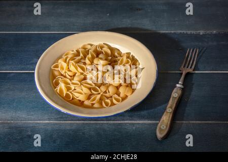Pasta-Kochkonzept. Frische hausgemachte Pasta in Muschelform serviert auf einem Teller auf blauem Holzhintergrund, Nahaufnahme Stockfoto