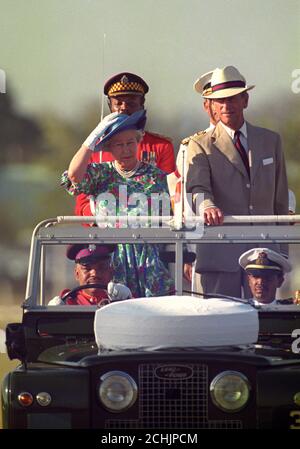 Königin Elizabeth II hält sich an ihrem Hut, als sie und der Herzog von Edinburgh in einem offenen Land Rover fahren, während sie Mitglieder des zweiten Bataillons des Jamaica Regiments während der Trooping the Color Zeremonie in Kingston, Jamaika, inspizieren. Stockfoto