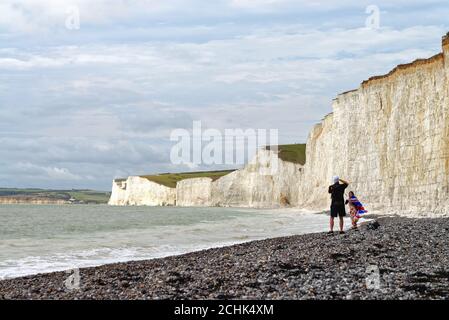 The Seven Sisters Kreidefelsen bei Birling Gap mit einem jungen Paar im Vordergrund, das den Blick vom Strand aus fotografiert, East Sussex England Stockfoto