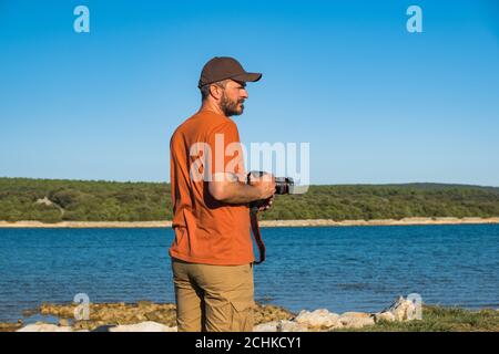 Fotograf Mann in T-Shirt und Cargo-Hosen zu Fuß rund um Meer Küste mit DSLR-Kamera und schießen Natur, Halbkörper Porträt, Landschaftsfotografie c Stockfoto