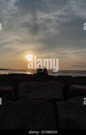 Junges Paar, das den Sonnenuntergang am Strand beobachtet Stockfoto