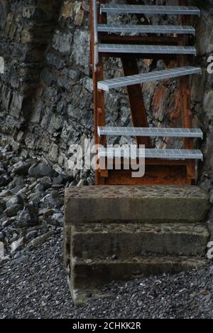 Vertikale Aufnahme einer rostigen und beschädigten Leiter an der Steinwand. Stockfoto