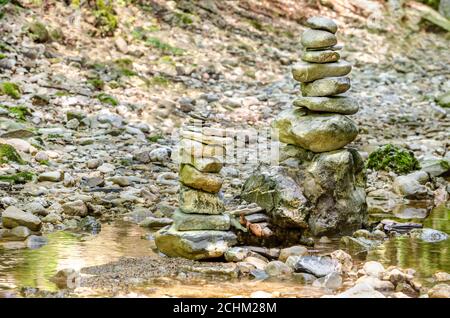 Rock Balancing. Zwei Stapel gestapelter Felsen in einem Flussbett. Felsen lagen flach aufeinander zu großer Höhe. Ausgewogene Felsen am Bach. Stockfoto