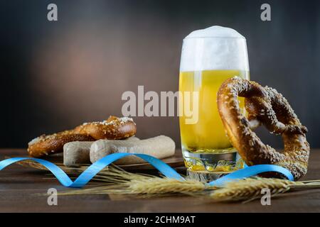 Becher helles Bier mit Schaumstoff, weiße bayerische Würste und Brezeln auf dem Holztisch, typisches Getränk und Snack am Oktoberfesttag. Stockfoto