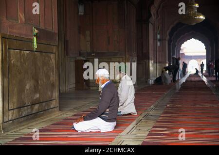 Delhi, Indien: Jama Masjid Moschee. Indische Männer beten vor einer Wand. Stockfoto