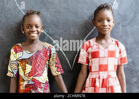 Wunderschöne afrikanische Schwestern posieren, lächeln und lachen glücklich vor der Tafel in der Schule Stockfoto
