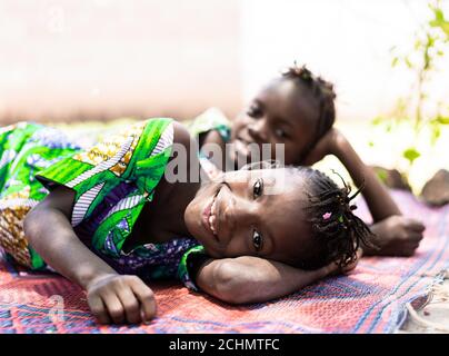 Lächelnde afrikanische Schwestern liegen auf dem Boden lächelnd und lachen fröhlich vor der Kamera Stockfoto