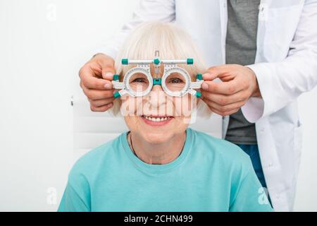 Lächelnde ältere Frau mit optometristischer Studie in der Augenklinik. Augenarzt bei der Auswahl von Brillen für die Behandlung des Sehvermögens Stockfoto