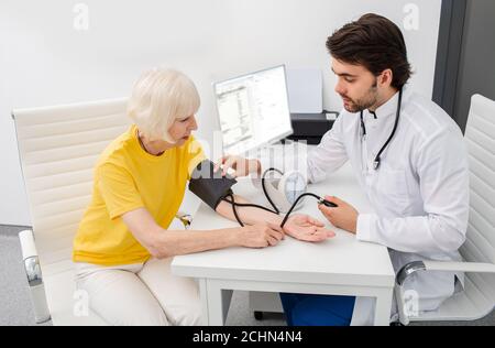 Arzttherapeutin in der modernen Klinik misst den Körperdruck einer Seniorin. Prävention von Erkrankungen der Hypertonie, Atherosklerose und Herzinsuffizienz Stockfoto