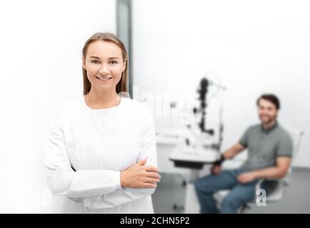 Porträt einer schönen Augenärztin in einem modernen Augenarztbüro sitzt im Hintergrund ein schöner männlicher Patient Stockfoto