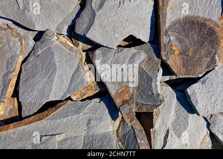 Struktur und Hintergrund von großen Brocken aus grauem felsigen Sandstein mit Rissen und rostigen Flecken in rauem Sonnenlicht. Stockfoto